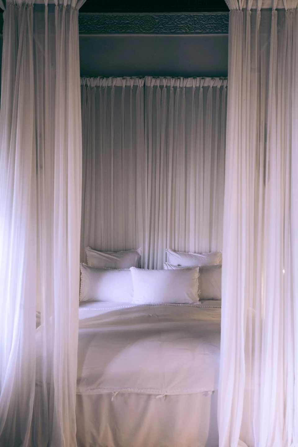 White bed linen behind sheer curtains in soft interior light