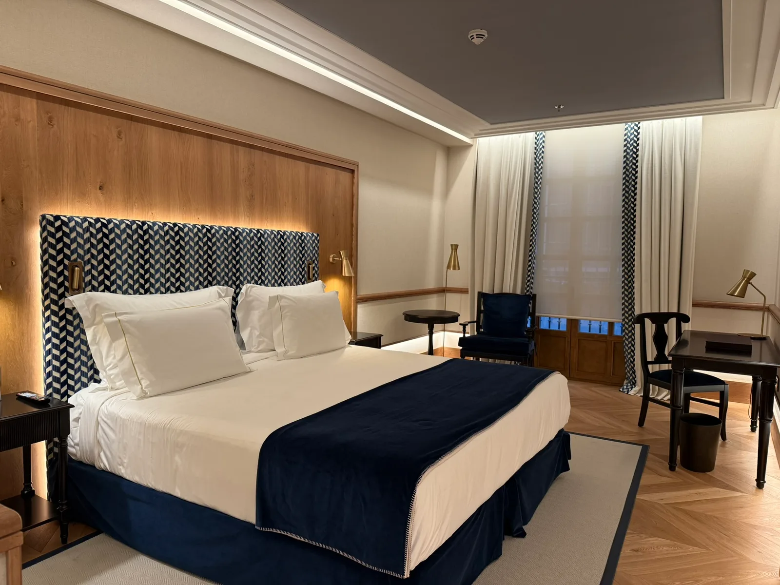 Guest room at Palacio Solecio in Málaga, with a blue patterned headboard, wooden panelling and parquet flooring.